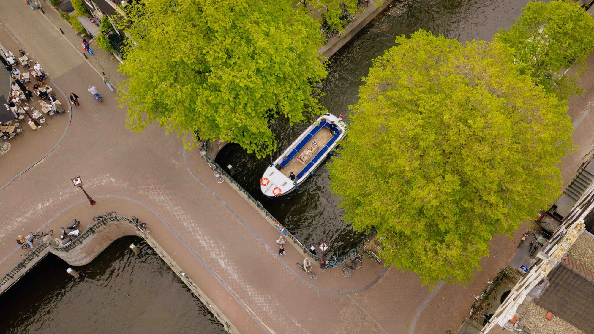 De Club Amstel boot van bovenaf tussen de groene bomen op de gracht